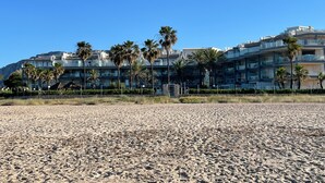 A beach with a row of multi-story buildings, palm trees, and a clear blue sky. - Apartment 'Residencial Mar De Denia 2' with Sea View, Wi-Fi and Air Conditioning (Denia)