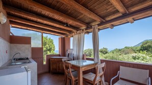 Una cocina con pileta y estufa, una mesa de comedor con sillas, y vistas a zonas verdes y colinas.