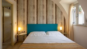 Un dormitorio con pared de listones de madera, cabecera color turquesa, colcha estampada, lámparas de noche y una ventana con cortinas.