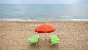 Una playa con dos sillas reclinables verdes y un paraguas rojo.