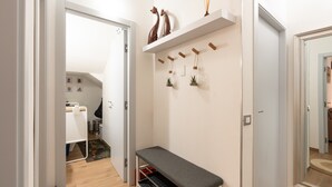 Um corredor com um banco, uma estante com objetos decorativos e uma porta que dá para outro quarto.