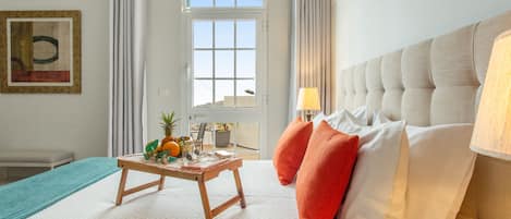 Habitación de hotel con una cama, una mesita con fruta, vista por la ventana y un cuadro en la pared.