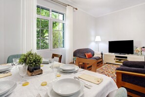 Un coin repas avec une table dressée pour quatre personnes, un téléviseur et une fenêtre donnant sur un paysage verdoyant.