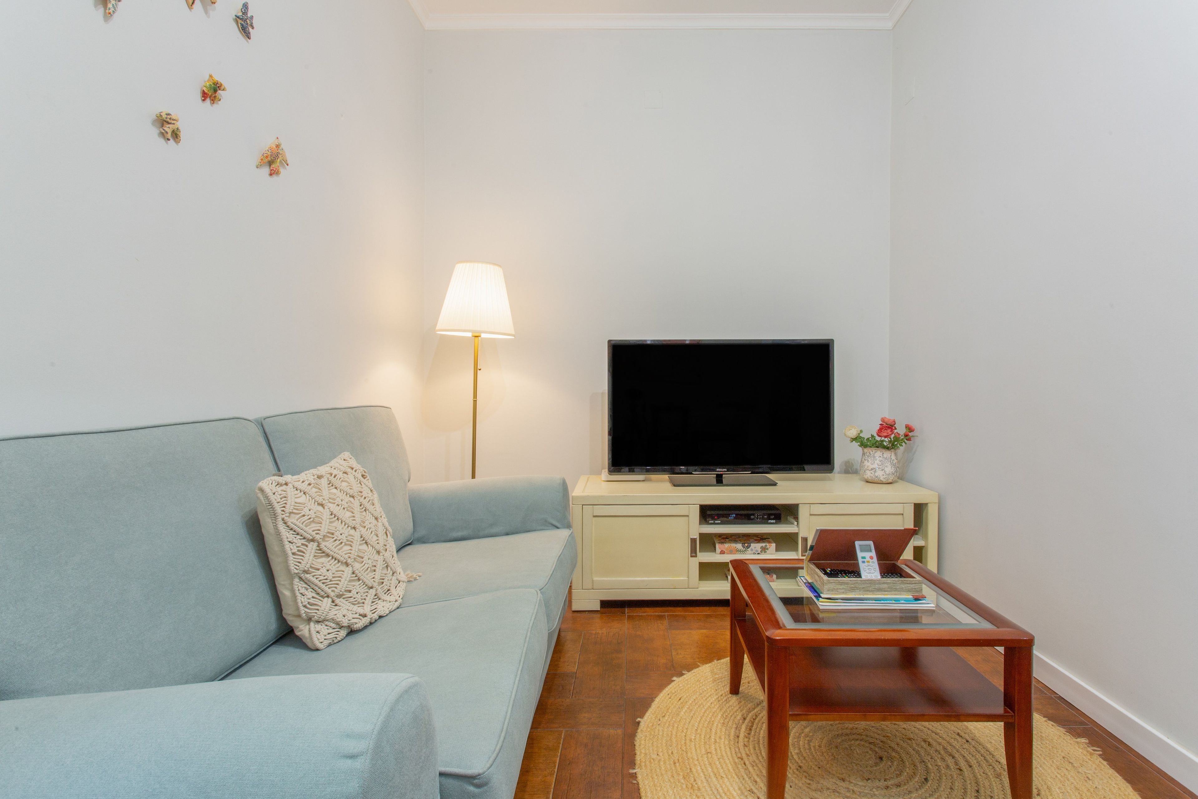 Uma sala de estar com sofá, televisão, abajur e mesa de centro.