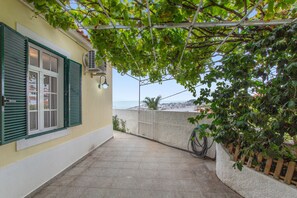 A covered outdoor area with a view of the sea, a bicycle, and a building with shutters. - A Minha Casa – Your Holiday Home in Funchal with Sea Views (Funchal)
