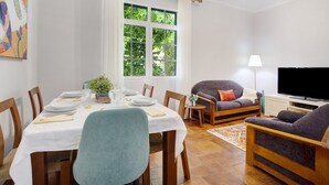 A dining area with a table set for four, a sofa, a TV, and a window with curtains.