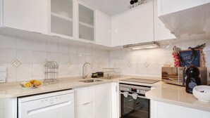 A modern kitchen with white cabinetry, a dishwasher, an oven, and a coffee maker.