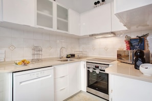 A modern kitchen with white cabinetry, a dishwasher, an oven, and a coffee maker.