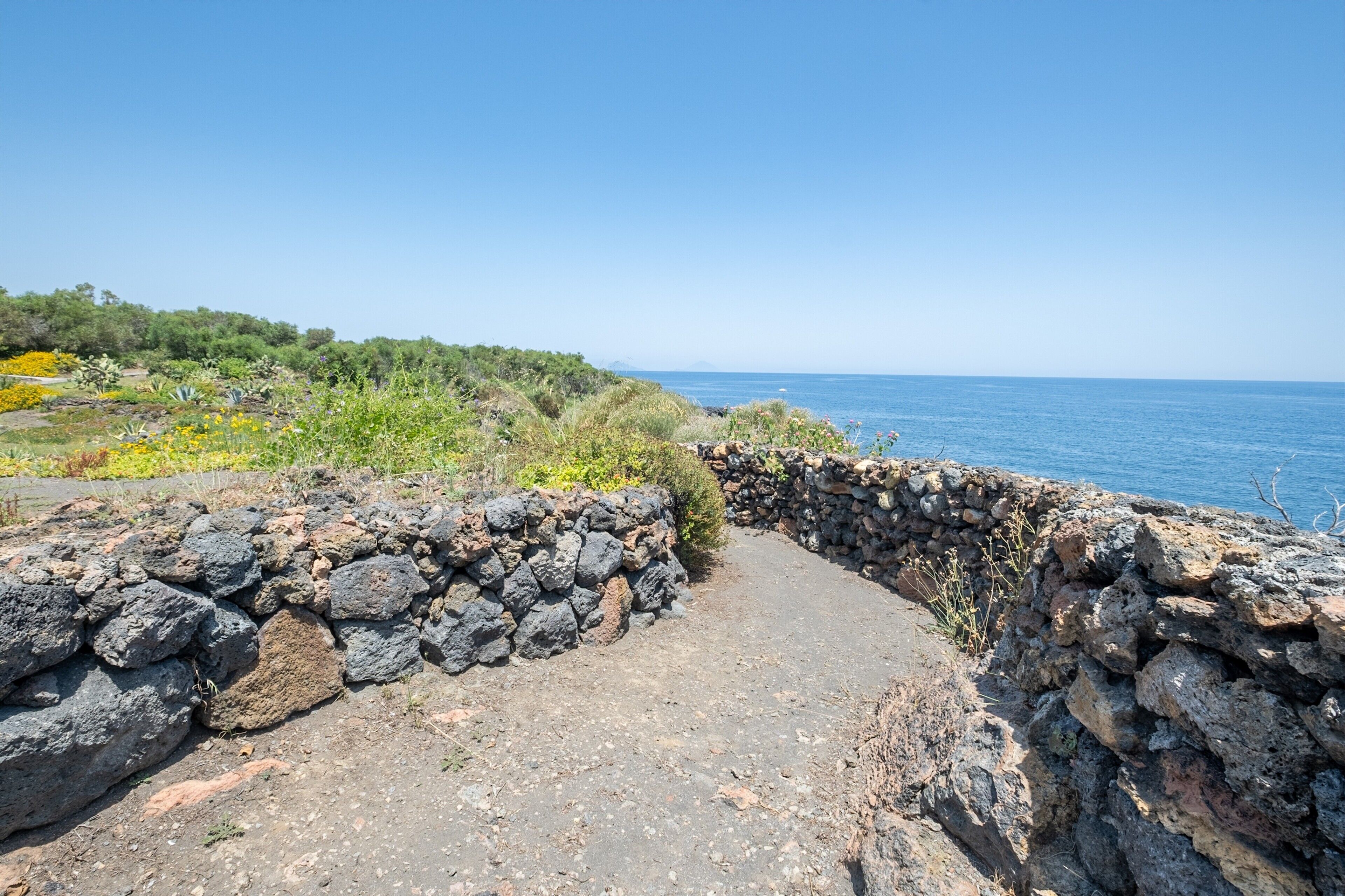 Un sendero costero con muros de piedra, que lleva al mar.