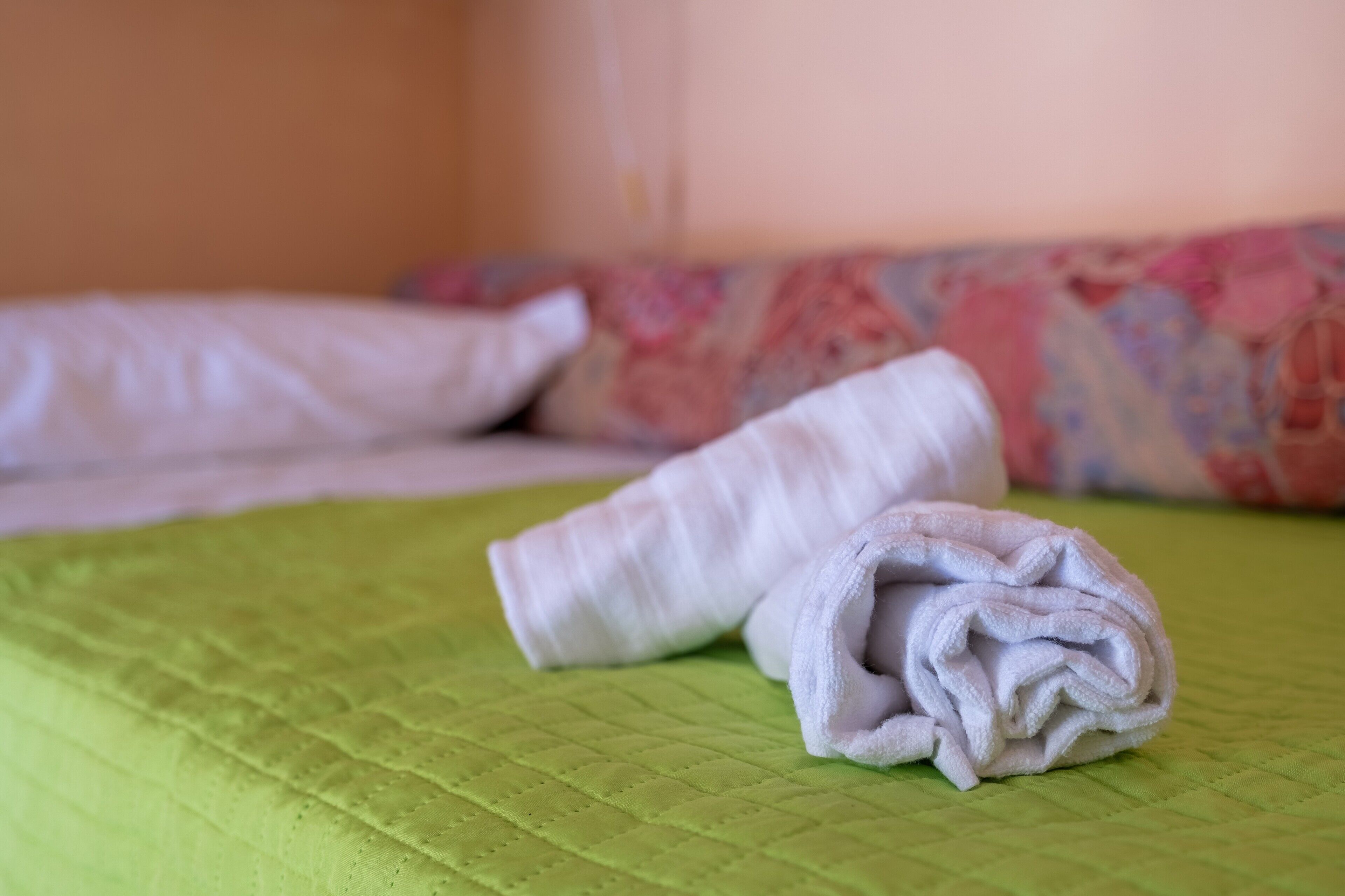 Una cama con un edredón verde acolchado y dos toallas blancas dobladas con cuidado.
