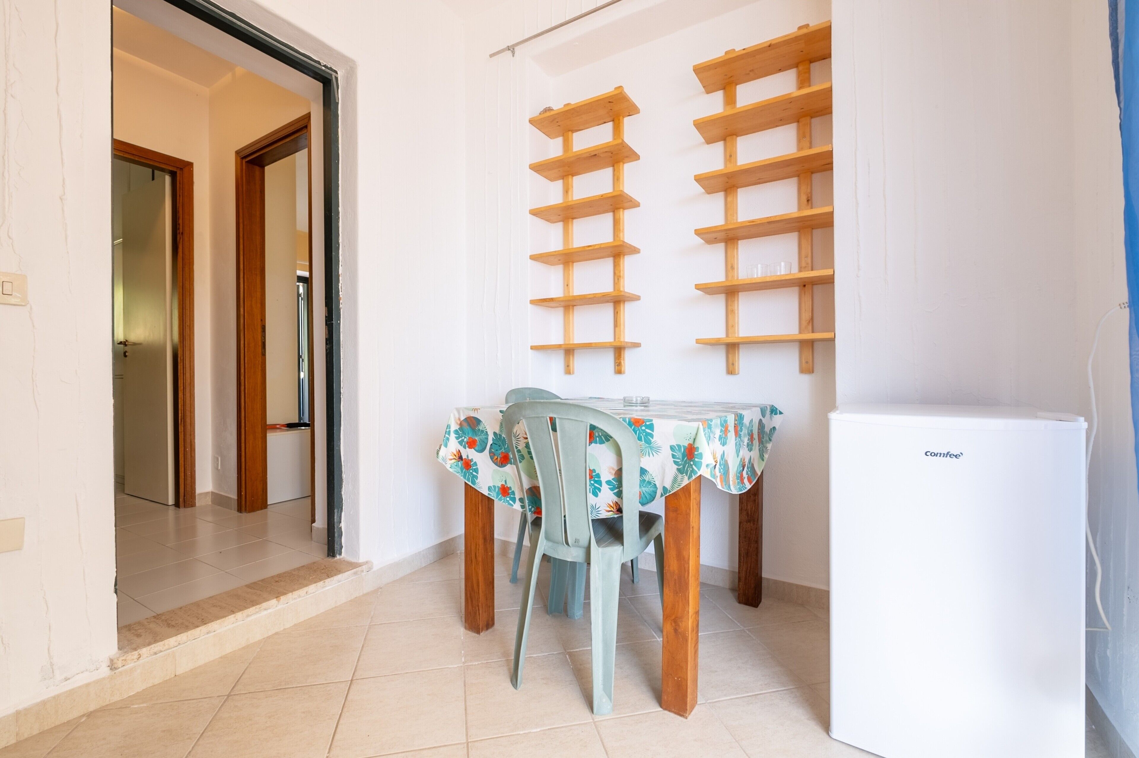 Un espace repas comprenant une table, des chaises, un réfrigérateur et des étagères en bois.