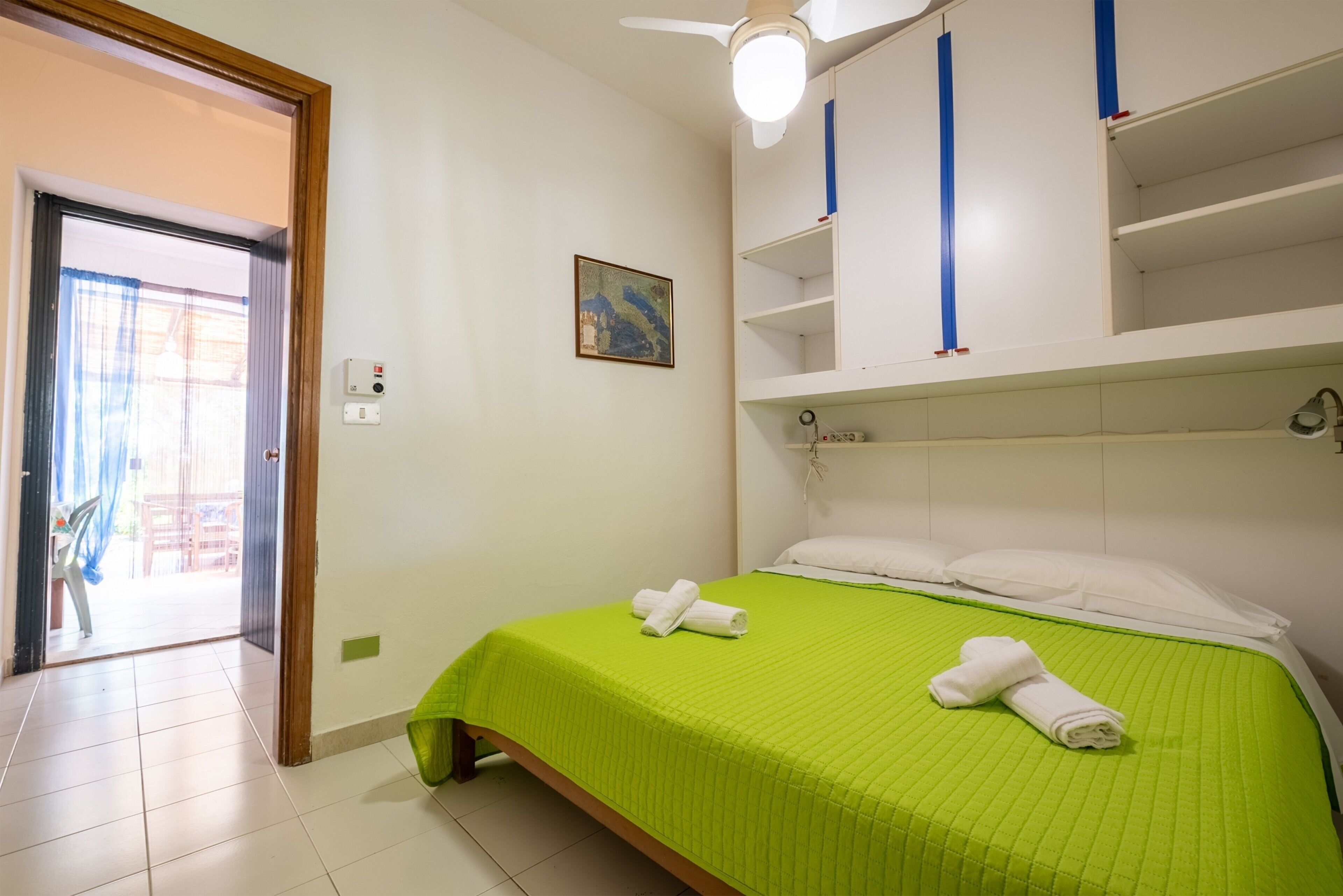 A hotel room with a bed, a ceiling fan, a painting, and a door leading to a balcony.