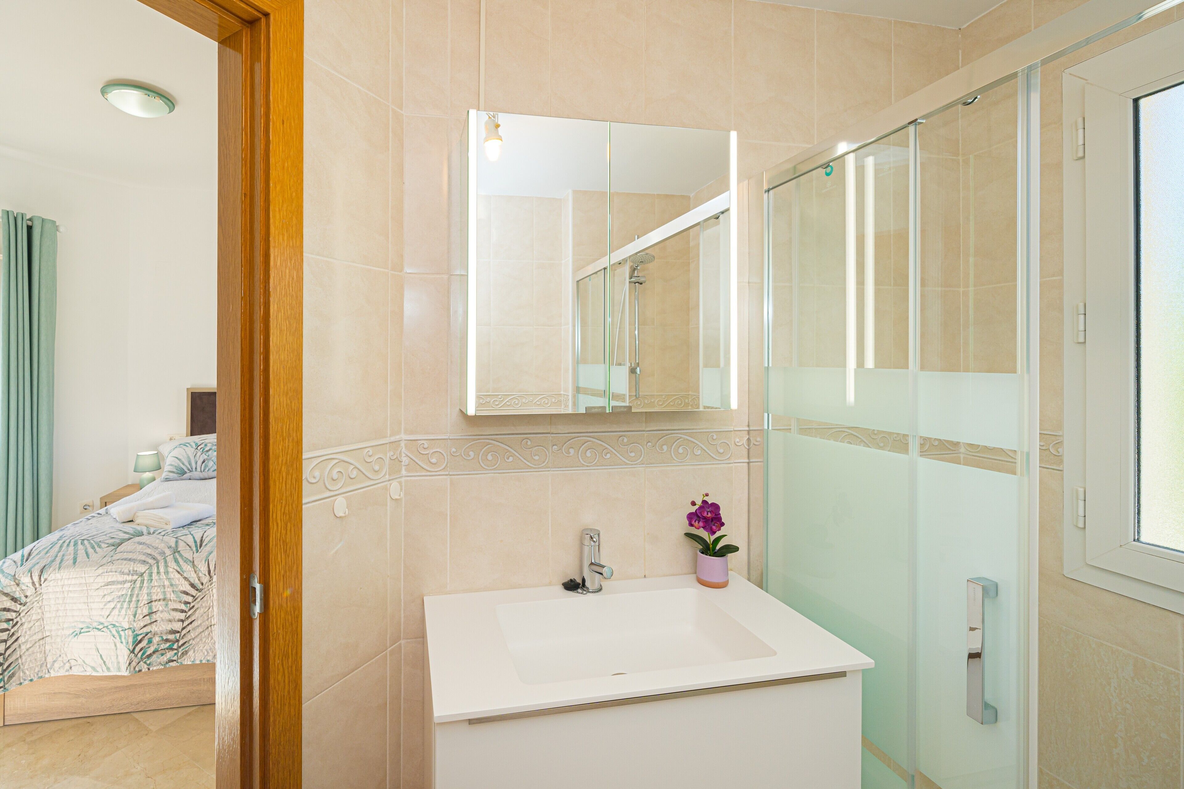 A bathroom with a sink, mirror, shower, and a potted orchid.
