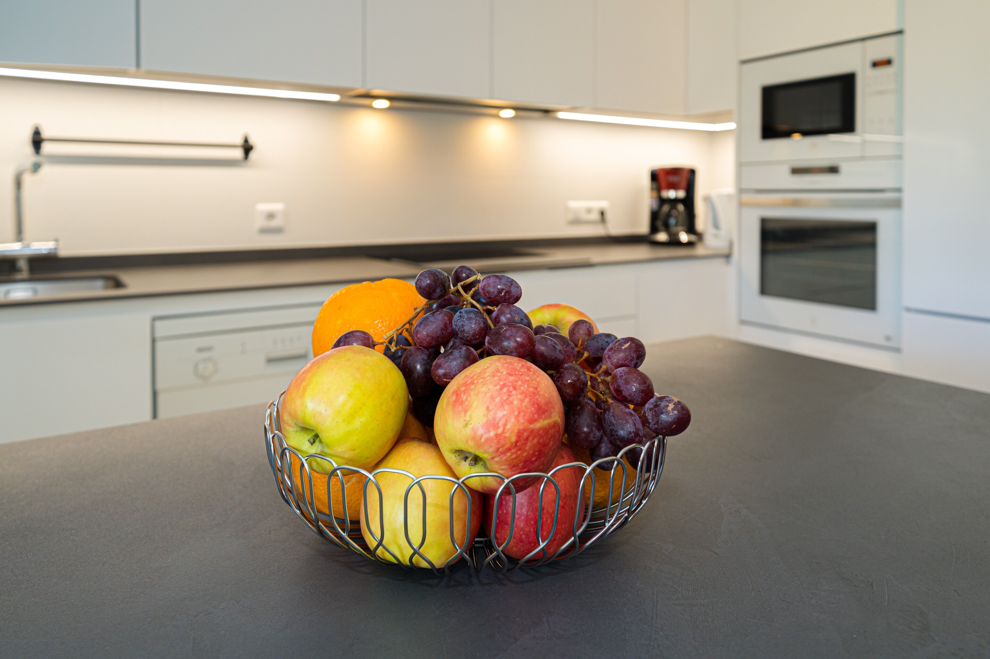 Une cuisine avec un panier de fruits sur le comptoir, un four à micro-ondes et un four traditionnel.