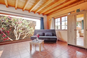 A room with a wooden ceiling, a grey sofa, a wooden cabinet, and a tiled floor.