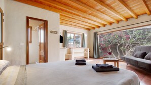 Quarto com cama, sofá, televisão e vista para árvores.
