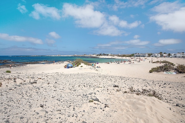 A beach with scattered rocks, a few umbrellas, and buildings in the background.