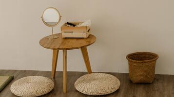 A small wooden table with a round mirror and a box containing tissues. There are two woven poufs and a woven basket on the floor.