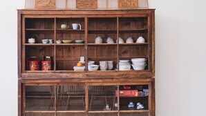 A wooden cabinet with multiple shelves containing various ceramic items, including cups, bowls, and plates. - TUNGWEI38 HOSTEL (Magong)
