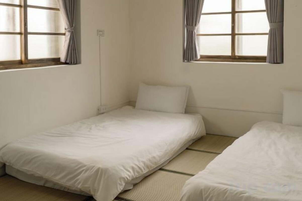 Une chambre avec deux lits simples, une fenêtre avec des rideaux et une prise électrique visible sur le mur.