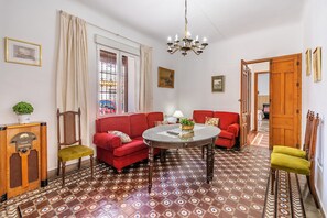 Una stanza con un divano rosso, un tavolo rotondo, un armadietto in legno e piastrelle a motivi decorativi.