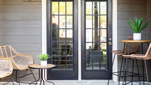 A black double door with a grid pattern, a small round table with a potted plant, and wicker chairs.