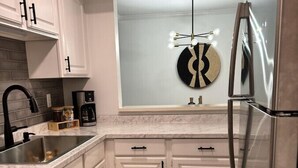 A modern kitchen with white cabinets, a stainless steel refrigerator, a coffee maker, and a unique wall art piece.