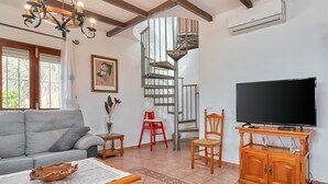 Ein Wohnzimmer mit einer Couch, einem Couchtisch, einem Fernseher auf einem Holzboden, einem roten Sessel, einer Wendeltreppe und einem Bild an der Wand.