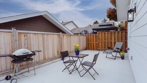 A backyard patio with a grill, folding chairs, and a table.