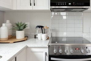 Cozinha com fogão de aço inoxidável, armários brancos e painel de azulejos.