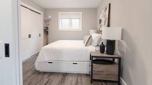 A bedroom with a bed, bedside table, lamp, and a window.