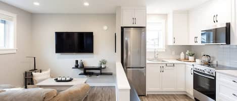 A modern kitchen with white cabinetry, a stainless steel refrigerator, a microwave, and an oven.