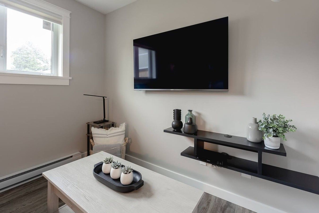 Een woonkamer met een flatscreen televisie aan de muur, een houten tafel met decoratieve objecten en een stoel.