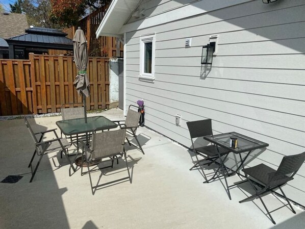 A patio with a table and chairs, a wooden fence, and a house with siding. - Charming Carriage Home (Victoria)