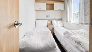 Une chambre à coucher de taille modeste, comprenant deux lits, une petite table de chevet, une armoire et une fenêtre avec des rideaux.