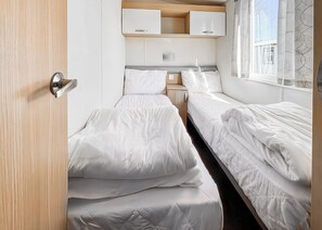 A compact bedroom with two beds, a small bedside table, a cabinet, and a window with curtains.