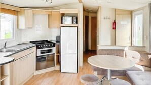 A compact kitchen with a stove, oven, and refrigerator, a dining area with a round table and stools, and a cozy seating area with a sofa.