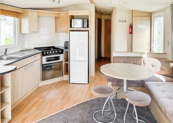 A compact kitchen with a stove, oven, and refrigerator, a dining area with a round table and stools, and a cozy seating area with a sofa.