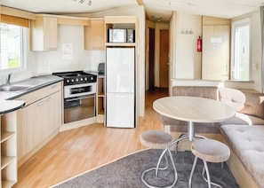 A compact kitchen with a stove, oven, and refrigerator, a dining area with a round table and stools, and a cozy seating area with a sofa.