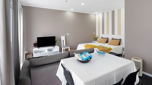 Una habitación de hotel moderna con sofá, mesa de comedor, televisor y cama con cabecera a rayas.