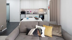 Una sala moderna con un sofá gris, una mesa de comedor y una cocina al fondo.
