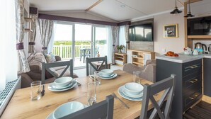 A modern kitchen with a flat-screen TV, dining area with a wooden table and chairs, and a balcony with a view. - 2 bedroom accommodation in Holywell Bay (Holywell Bay)