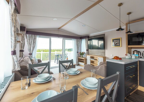 A modern kitchen with a flat-screen TV, dining area with a wooden table and chairs, and a balcony with a view.