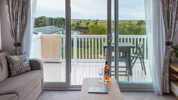 A room with a sliding glass door leading to an outdoor deck with a view of a green landscape. - 2 bedroom accommodation in Holywell Bay (Holywell Bay)