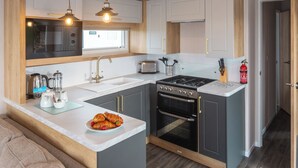 A modern kitchen with a central island, a stove, oven, and a microwave. - 2 bedroom accommodation in Holywell Bay (Holywell Bay)