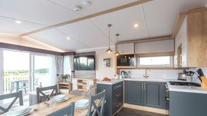 A modern kitchen with a dining area, large windows, and a view of the outdoors. - 2 bedroom accommodation in Holywell Bay (Holywell Bay)