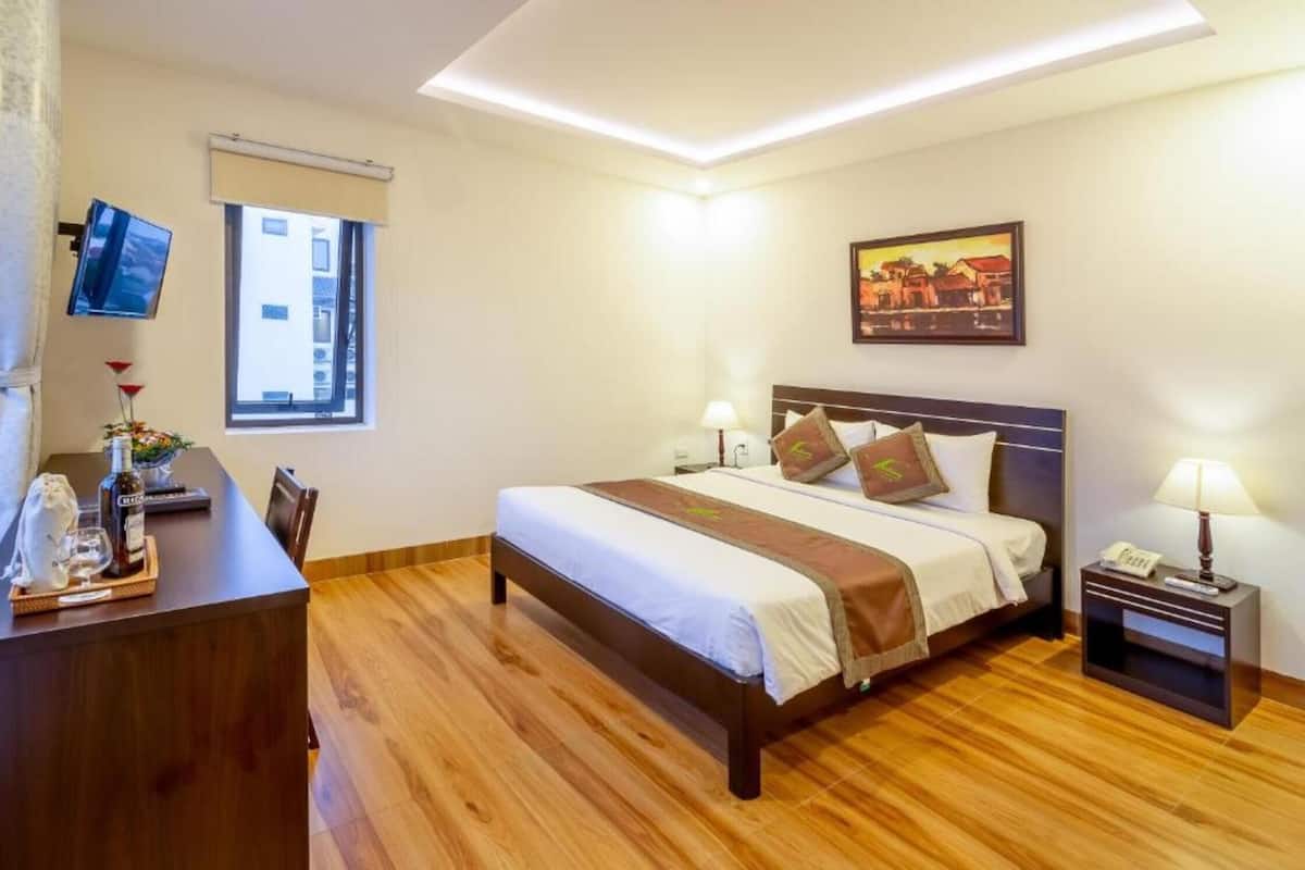 Ein Hotelzimmer mit Bett, Nachttischen, einem Schreibtisch, einem Fernseher, einem Fenster und einem Bild an der Wand.