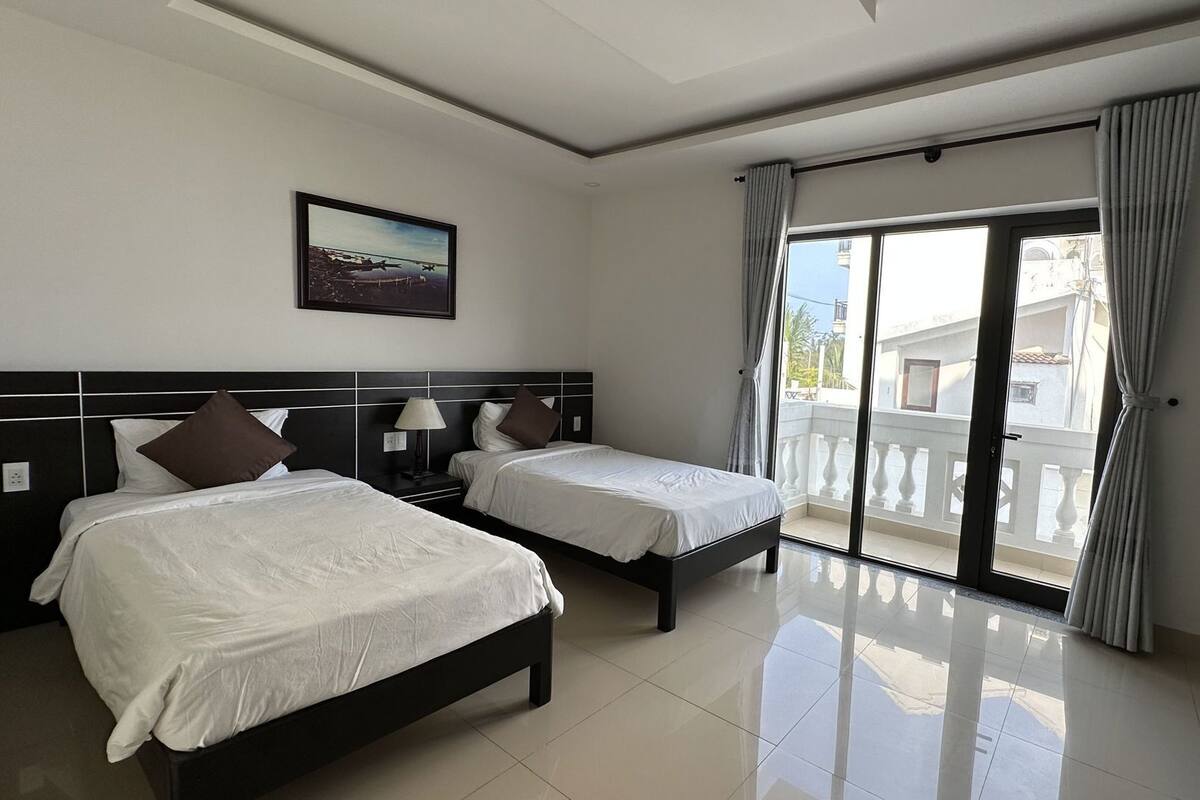 Ein Hotelzimmer mit zwei Betten, einem Bild an der Wand und einem Balkon mit Vorhängen.