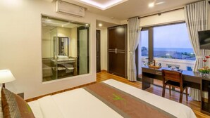 Una camera d'albergo con un letto, una scrivania, una sedia, una televisione, un armadio e un'ampia finestra con vista.