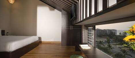 A modern bedroom with a wooden floor, a bed, a green ottoman, a window with a view of the city, and a ceiling with exposed beams.